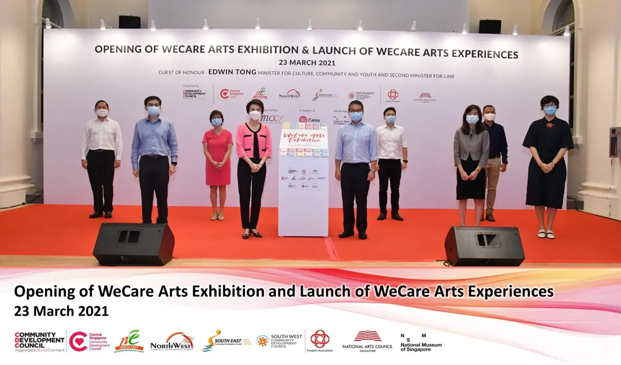 Group standing on a red carpet stage at the opening of WeCare Arts Exhibition and Launch of WeCare Arts Experiences.